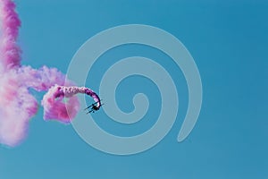 Aerobatic plane leaving a pink smoke trail in the blue sky.