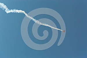 Aerobatic plane leaving a white smoke trail in the blue sky.