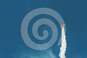 Aerobatic plane leaving a white smoke trail in the blue sky.