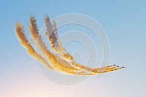 Aerobatic team group of fighters jet flies in the sky with brightly colored smoke under the setting sun in the evening sky