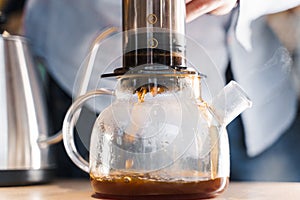 Aeropress coffee and glass pot close-up: barista press to device and coffee drops pours trought aeropress to pot