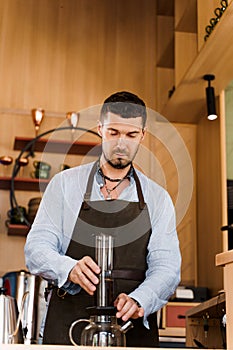 Aeropress coffee and handsome bearded barista in cafe. Barisa cook tasty coffee using alternative brewing method.