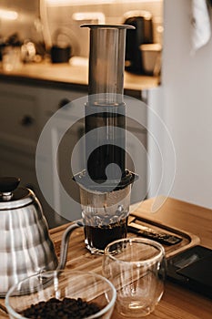 Aeropress and glass cup, scales, manual grinder, coffee beans, kettle on wooden table. Professional barista preparing coffee by