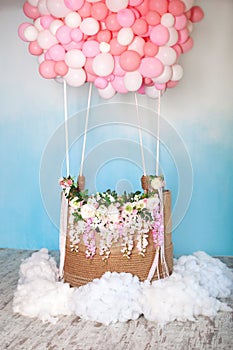Aerostat from balloons with basket decorated with flowers. Balloons basket for air flight on background decorative blue sky with c