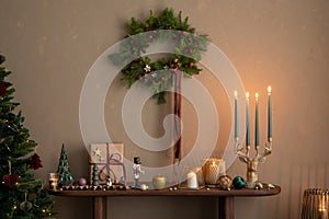 Aesthetic composition of christmas living room interior with wooden console, christmas gifts, candle with candlestick, christmas