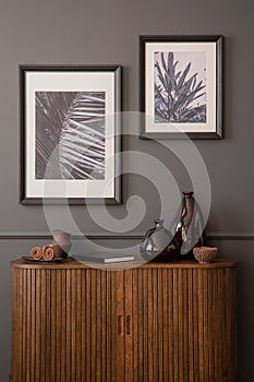 Aesthetic composition of living room interior with mock up posters frame, stylish wooden sideboard, glass vase, book, gray wall