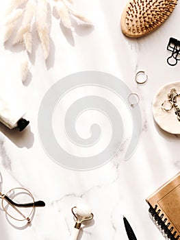 Aesthetic composition with modern notebook, stationery, fashion accessories and dry plants on white marble table with shadows