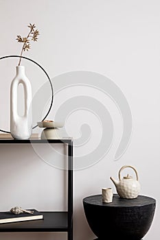 Aesthetic interior of living room with copy space, white wall, round black coffee table, simple console with stylish accessories.