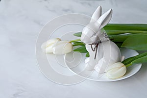 Aesthetic minimal Easter holiday decoration, white porcelain bunny figurine on plate, tulip flowers on neutral marble