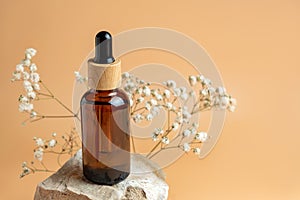 Aesthetic minimalist beauty care concept. Organic serum oil cosmetics bottle made of dark glass on stone with flowers