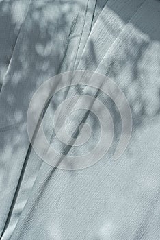 Aesthetic natural textile background with abstract sunlight shadow, neutral light blue draped fabric, copy space