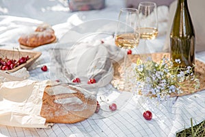 Aesthetic picnic outdoors with wine glasses bread berries and flowers. Rustic picnic with neutral tones colours.