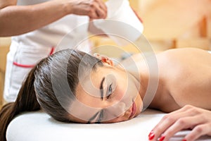 Aesthetician applying a transparent gel with spatula before laser epilation on female client legs in beauty salon.