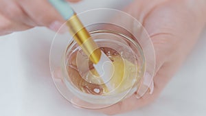 aesthetician mixing cream and facial mask in little bowl, closeup view of hands, serum for skin
