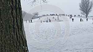 From afar view. Crowd of people  having fun In cold winter day and rides on an ice slide
