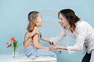 Affable female doctor examining tonsils of a happy little girl. Side view