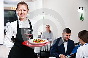 Affable female waiter is standing with order in luxury restaurante