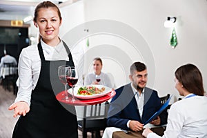 Affable female waiter is standing with order in luxury restaurante