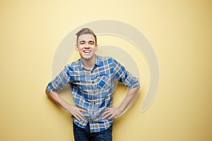 Affable guy dressed in a plaid shirt and jeans is sitting on a yellow background in the studio