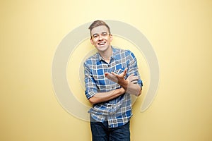 Affable guy dressed in a plaid shirt and jeans is standing on a yellow background in the studio