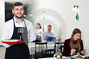 Affable male waiter is standing with order in luxury restaurante