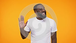 Affable young black man waving hand neighborly, isolated on yellow background