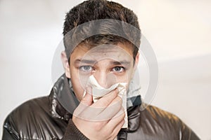 Affected by cold boy wipes his nose with handkerchief on gray background