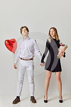 Affection. Young lovely couple connected by chains with balloons and flowers looking to each other with against studio photo