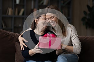 Affectionate adult daughter embrace excited older mother give birthday present