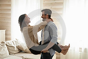 Affectionate boyfriend holds smiling girlfriend in arms lifting in air