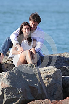 Affectionate couple flirting and hugging on a stone on the beach