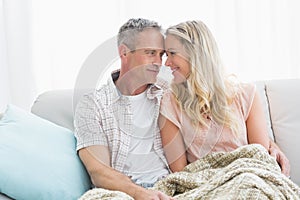 Affectionate couple sitting on sofa under blanket