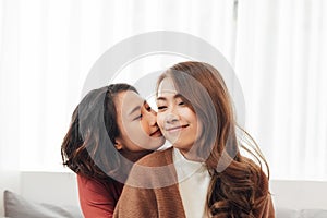 Affectionate girl kissing her happy sister or friend in the living room at home with a homey background