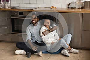 Affectionate happy african spouses cuddle on floor at modern kitchen