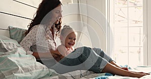 Affectionate Latina mom tickle cuddle little kid girl on bed