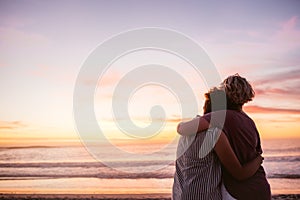 Affectionate lesbian couple watching the sunset by the ocean