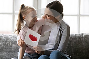 Affectionate loving mother embracing little daughter, reading congratulations in card.