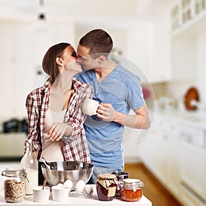 Affectionate man kissing his girlfriend while cutting bread for breakfast in the kitchen