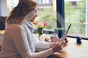 Affectionate mature woman using tablet during breakfast in cafe