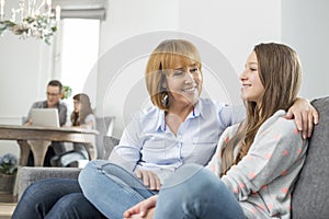 affectionate mother and daughter sitting on sofa with family in background