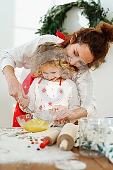 Affectionate mother helps her dughter to whisk eggs in bowl, stand together on kitchen, bake delicious pie for all