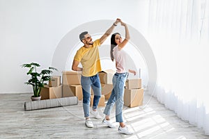 Affectionate multiracial couple dancing in their house among carton boxes on moving day, free space
