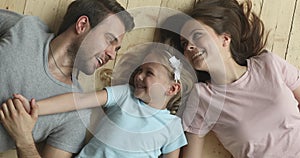 Affectionate parents and kid daughter laughing lying on warm floor