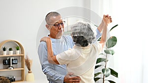 Affectionate senior couple dancing in living room, enjoying retired life and spending free time together at home