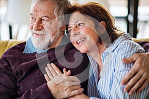 An affectionate senior couple in love sitting on sofa indoors at home.