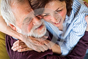 Affectionate senior couple in love sitting on sofa indoors at home, hugging.