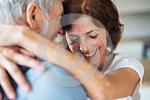 Affectionate senior couple in love standing indoors at home, hugging.