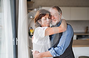 Affectionate senior couple in love standing indoors at home, hugging.