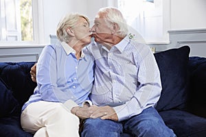 Affectionate Senior Couple Sitting On Sofa At Home