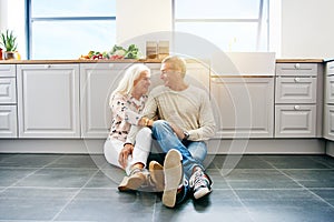 Affectionate senior couple sitting together on their kitchen flo